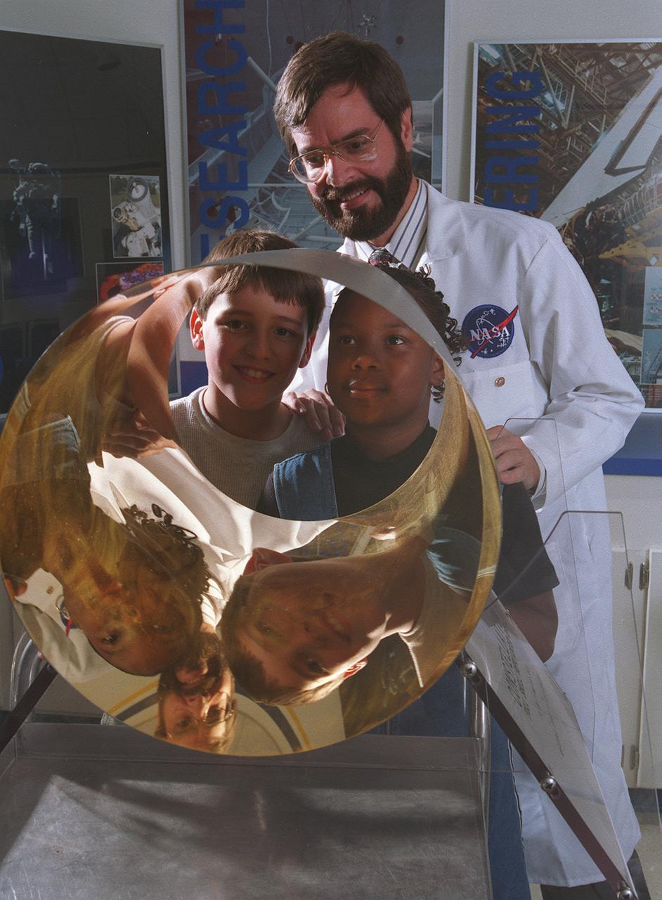 NASA educator showing students a reflective research material exhibit, illustrating science education and knowledge transfer.
